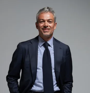 "Filippo Battistini, dirigente di AllianzGI, in abito scuro con camicia a righe e cravatta, posa sorridente su sfondo neutro."