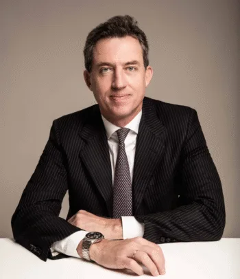 Ritratto professionale di Paolo Paschetta, responsabile Italia di Pictet AM in abito elegante, seduto a un tavolo, con espressione sicura e rilassata.