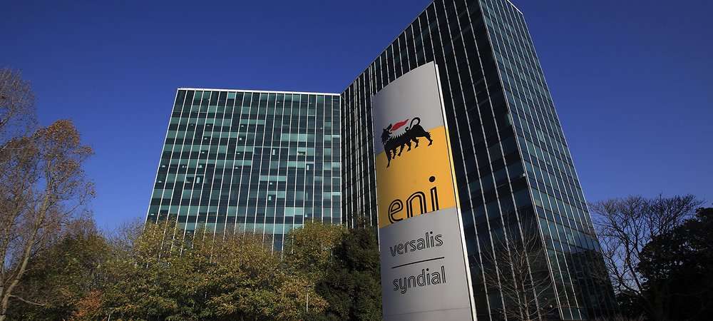 Sede principale di Eni a San Donato Milanese con logo aziendale visibile, grattacielo moderno circondato da alberi in una giornata di sole con cielo blu.