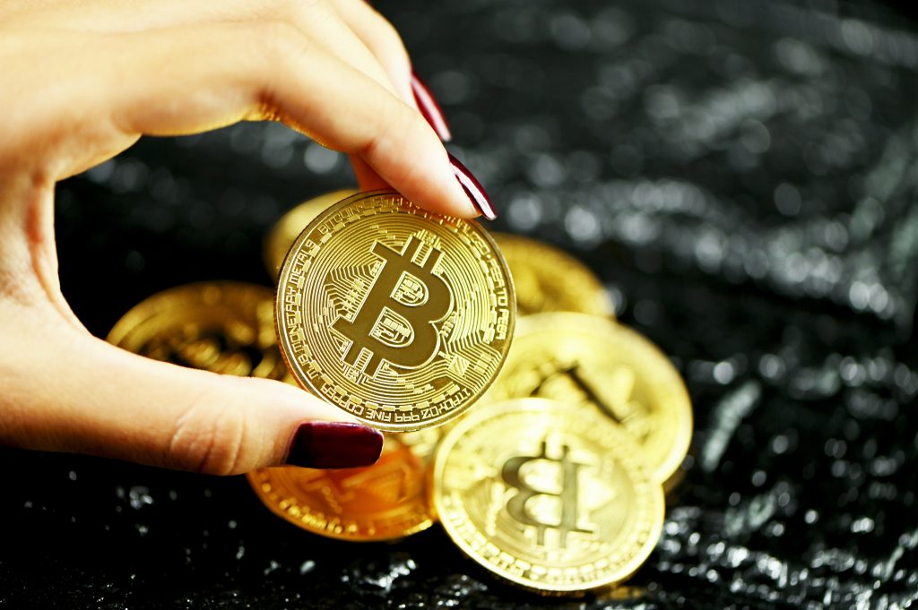 Una mano con le unghie dipinte di nero solleva un bitcoin