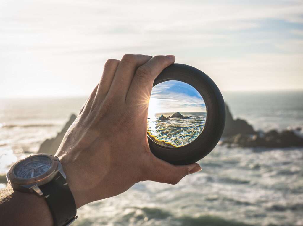 Una lente focale, tenuta da una mano, permette di inquadrare un particolare di un panorama marino