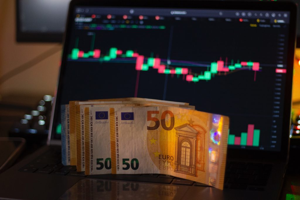 Una serie di banconote da 50 euro poggiata in davanti a un laptop che mostra il grafico a candele del cambio eur/usd