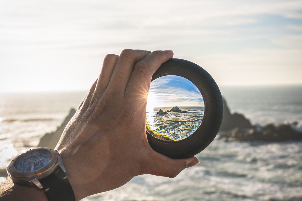 Un obiettivo fotografico tenuto da una mano permette di mettere a fuoco un panorama di mare