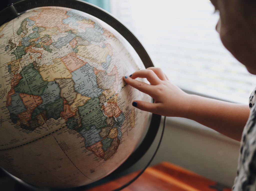 Un bimbo indica con la mano un punto su un mappamondo
