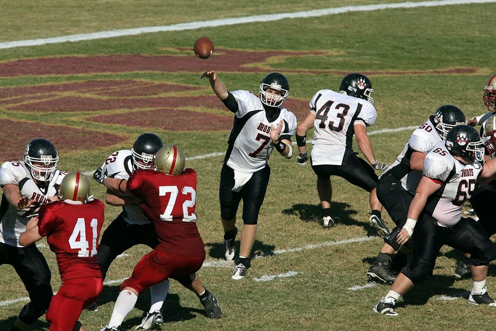 Una immagine tratta da una partita di football americano. Il quarter back lancia il pallone protetto dalla sua difesa