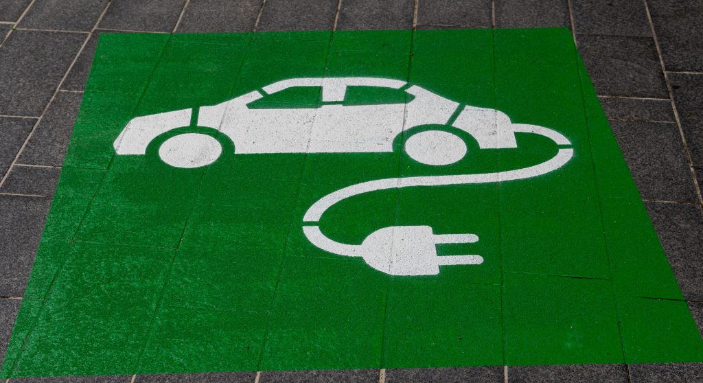 Un parcheggio riservato alle auto elettriche segnalato sull'asfalto da un disegno su sfondo verde.