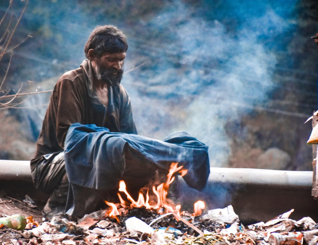 Un povero cerca di scaldarsi con un fuoco acceso per strada e una coperta