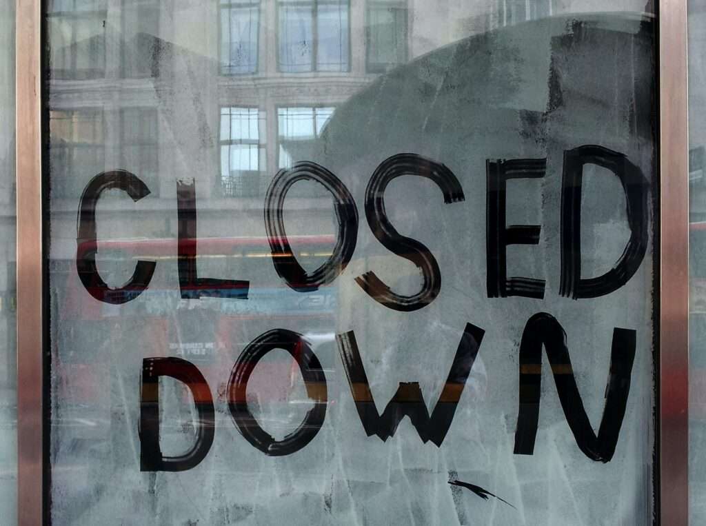 La porta a vetri di un negozio, dipinta di bianco per non mostrare l'interno e con la scritta: closed down