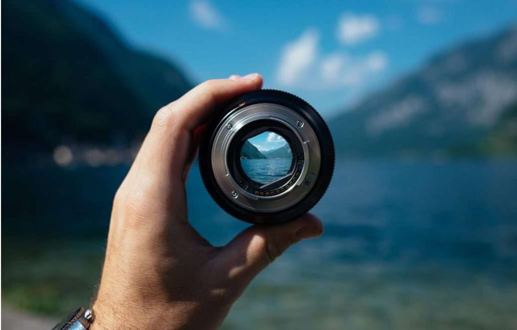 Un obiettivo tenuto da una mano inquadra e rende nitido il panorama sottostante