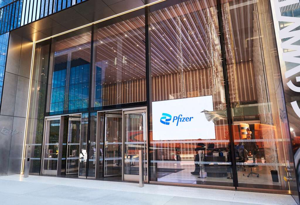 L'ingresso del quartier generale di Pfizer. Un'ampia vetrata con un cartello luminoso riportante il logo dell'azienda in celeste su sfondo bianco