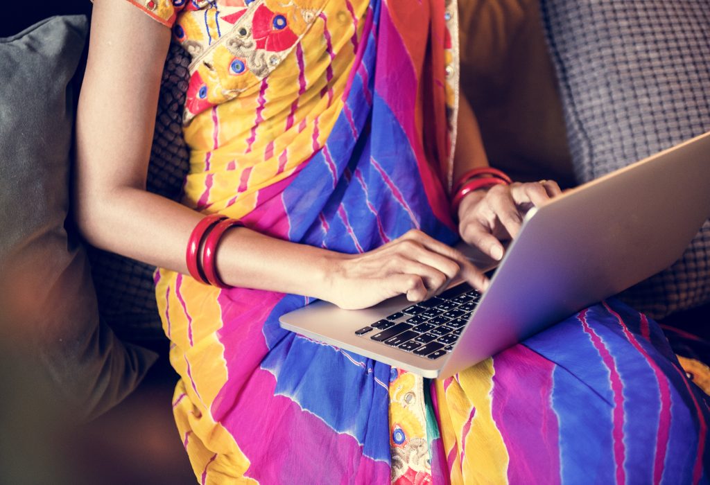 Una donna indiana in un colorato abito tradizionale utilizza un laptop - foto di Rowpixel, Envato