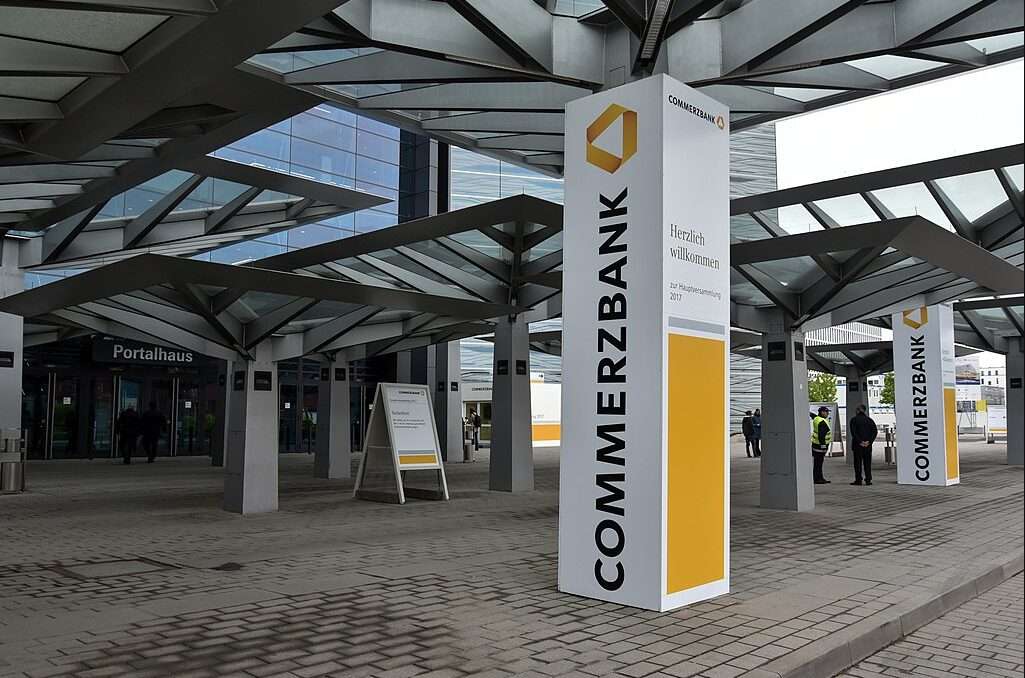 L'immagine mostra l'esterno della sede dove si è svolta l'assemblea generale degli azionisti di Commerzbank. È presente un parallelepipedo verticale con la scritta Commerzbank dal basso verso l'altro nei colori aziendali: giallo, nero e bianco