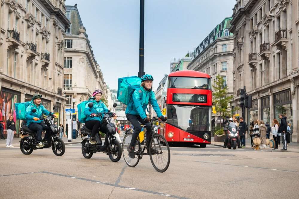 Nell'immagine, tre rider su biciclette e motorini per le strade di Londra effettuano consegne per Deliveroo