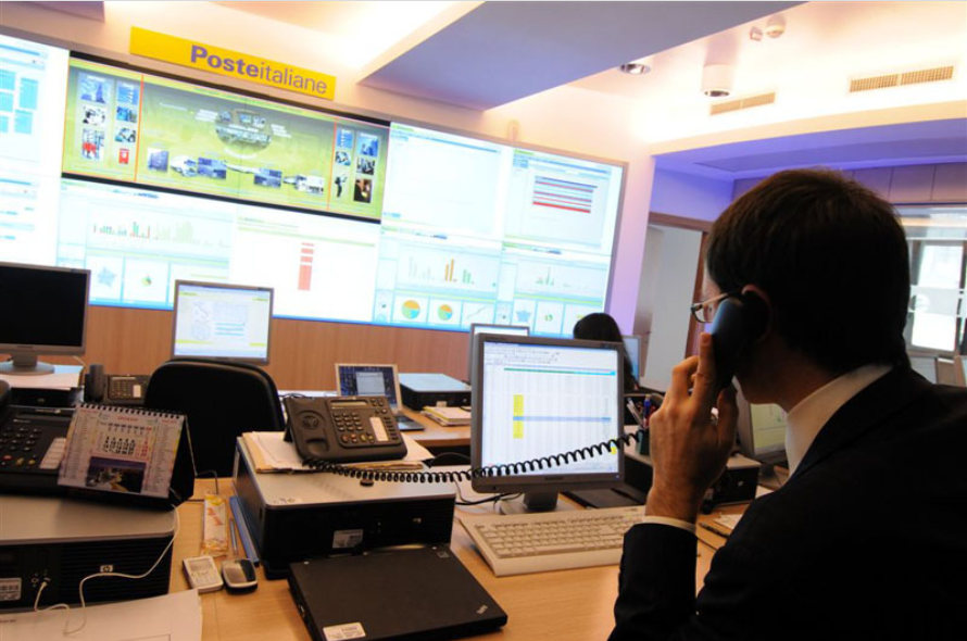 Nell'immagine una sala con computer e un megaschermo per le attività di controllo di Poste Italiane
