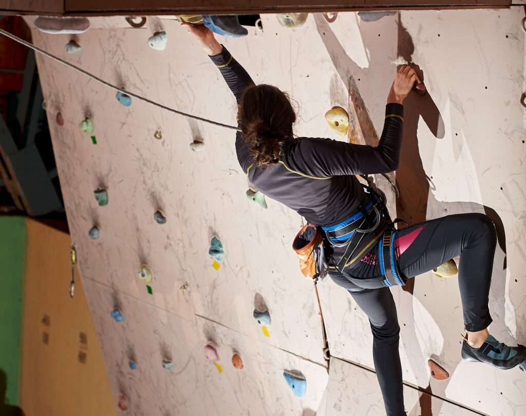 Nell'immagine una donna scala una parete in una palestra per climbing
