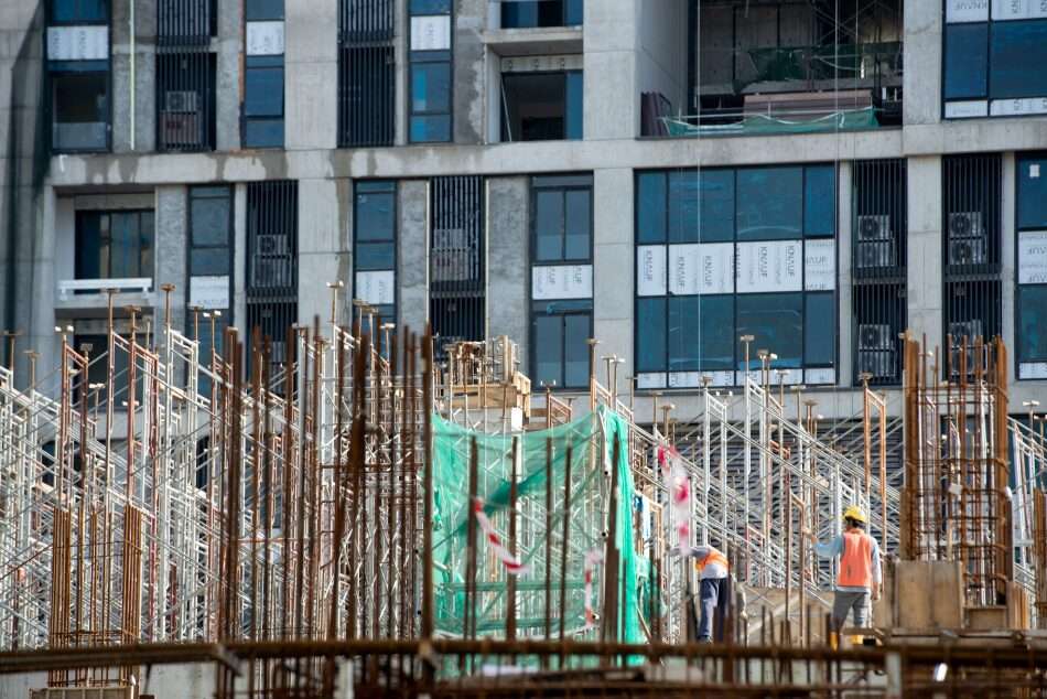 Nell'immagine due operai in un sito di un palazzo in costruzione, in mezzo ai rinforsi in acciaio