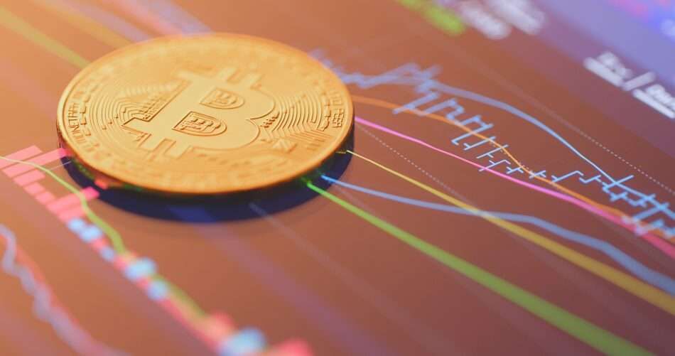 L'immagine mostra una moneta di bitcoin poggiata su uno schermo che riproduce un grafico di Borsa