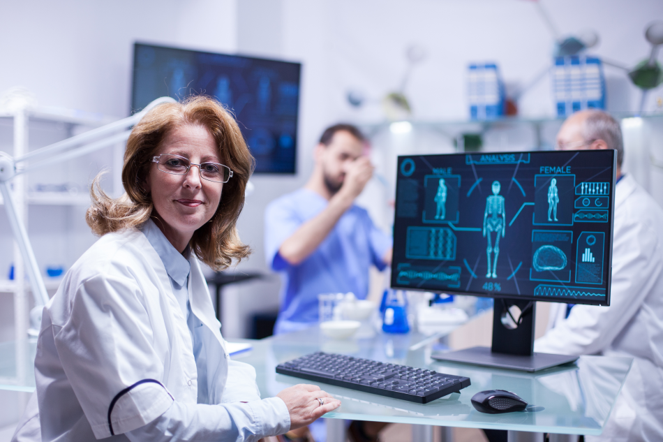 L'immagine mostra un ricercatrice in camice bianco in un laboratorio, seduta davanti a un computer che riportauna schematizzazione del corpo umano
