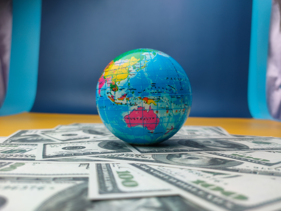 Un mappamondo è poggiato su delle banconote in dollari su un tavolo