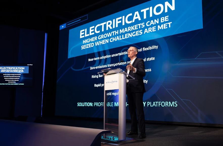 L'amministratore delegato di Stellantis sul palco dell'Investor day 2024, mentre parla di elettrificazione come recita lo schermo sullo sfondo