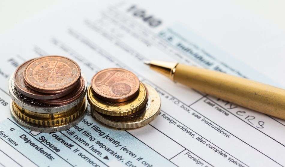 Alcune monete euro e una penna sono poggiate su un modulo per la dichiarazione dei redditi