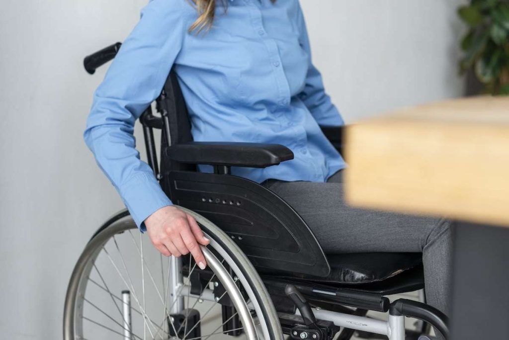 Persona in sedia a rotelle con camicia azzurra in un ambiente interno, rappresentazione della disabilità e mobilità ridotta, titolare di Legge 104.