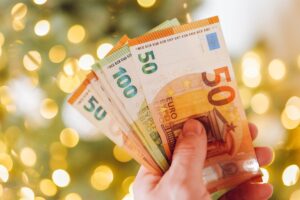 Banconote euro in mano con sfondo natalizio, informazioni sul Bonus Natale 2024