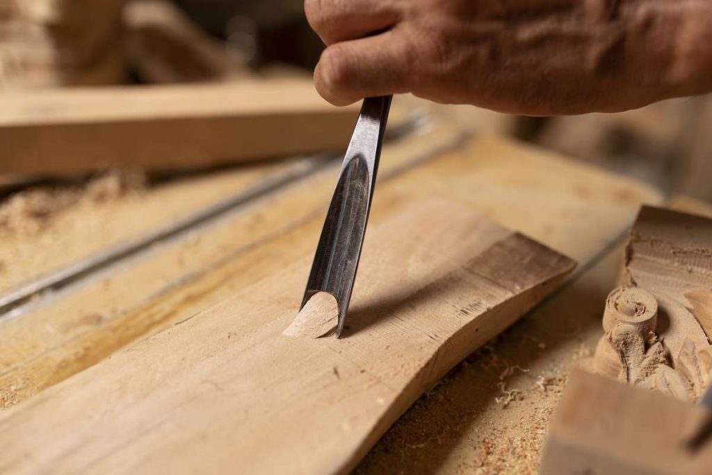 Mano di un falegname che utilizza uno scalpello su un pezzo di legno, eseguendo una lavorazione di precisione