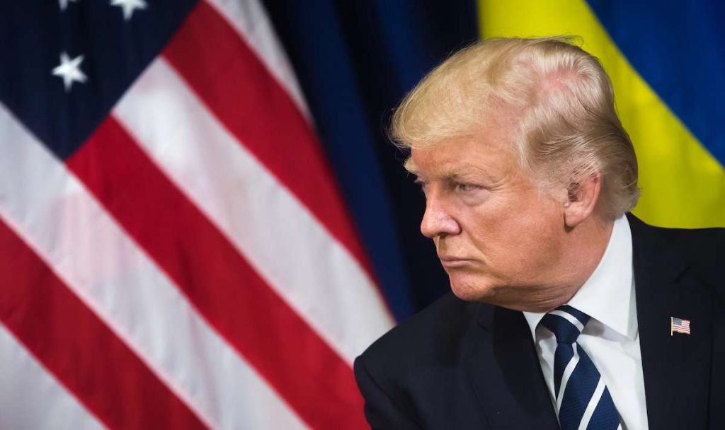 Donald Trump in abito scuro di profilo, con bandiera americana sullo sfondo. Immagine rappresentativa della politica USA e dei possibili candidati per il governo Trump, tra cui Elon Musk, Robert F. Kennedy Jr., e altri papabili nomi