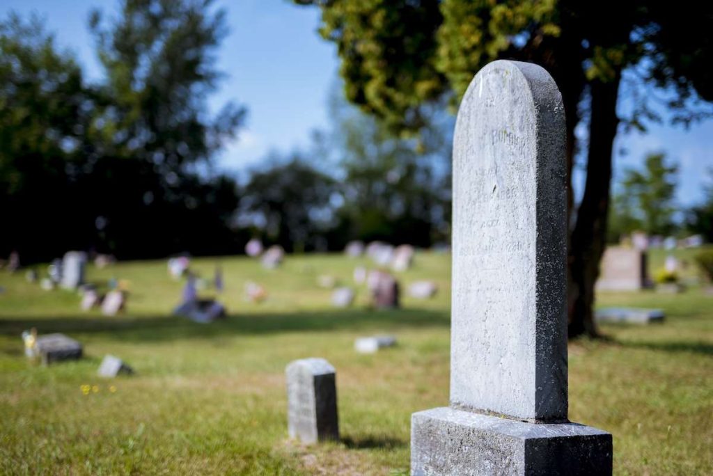 Lapide in un cimitero circondata da altre tombe su un prato verde. Immagine simbolica delle spese funebri e dei servizi cimiteriali, utile per articoli su agevolazioni fiscali e IVA applicabile alle spese funebri.