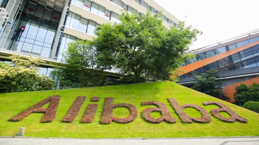 Vista della sede centrale di Alibaba Group, con il logo aziendale in erba verde su un prato ben curato e l'edificio moderno in vetro e acciaio sullo sfondo, situato a Hangzhou, Cina.