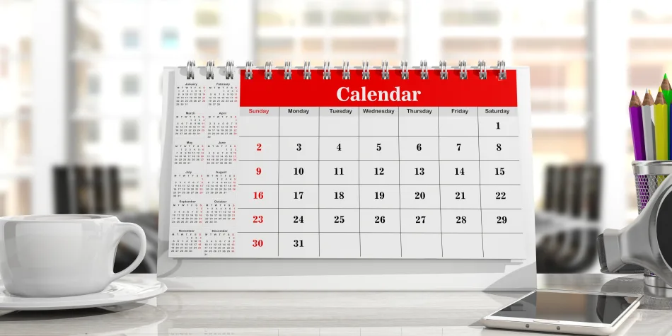 L'immagine mostra un calendario del 2025 poggiato su una scrivania. Accando al calendario, una tazza bianca