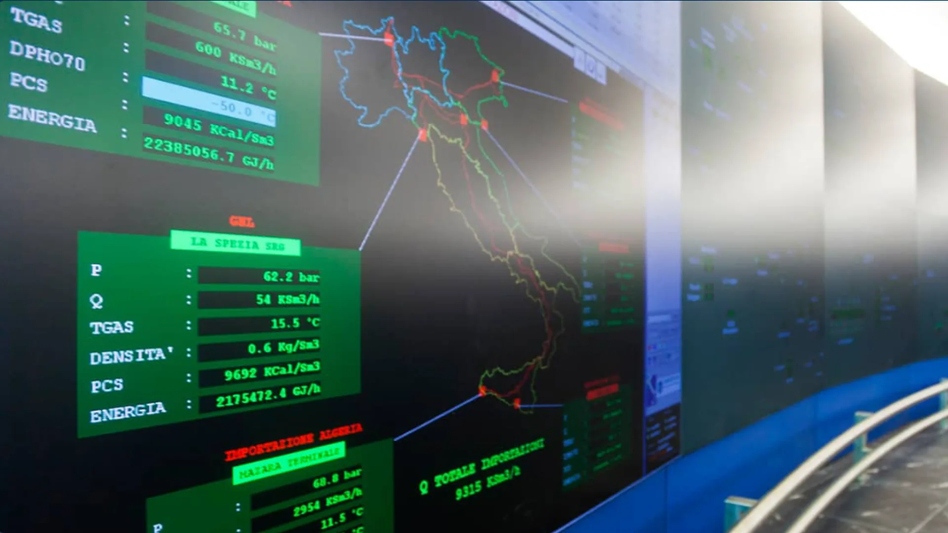Centro di controllo Snam con display digitale che mostra dati sul monitoraggio della rete del gas in Italia, incluse temperature, pressioni e volumi. La mappa centrale evidenzia i flussi di trasporto del gas naturale lungo il territorio italiano, con valori numerici di pressione e portata visualizzati a fianco