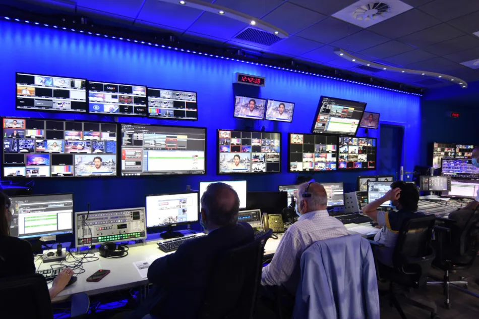 Sala di controllo televisiva con tecnici al lavoro presso gli studi di Milano di MFE Mediaset, con numerosi schermi e attrezzature per la gestione delle trasmissioni.