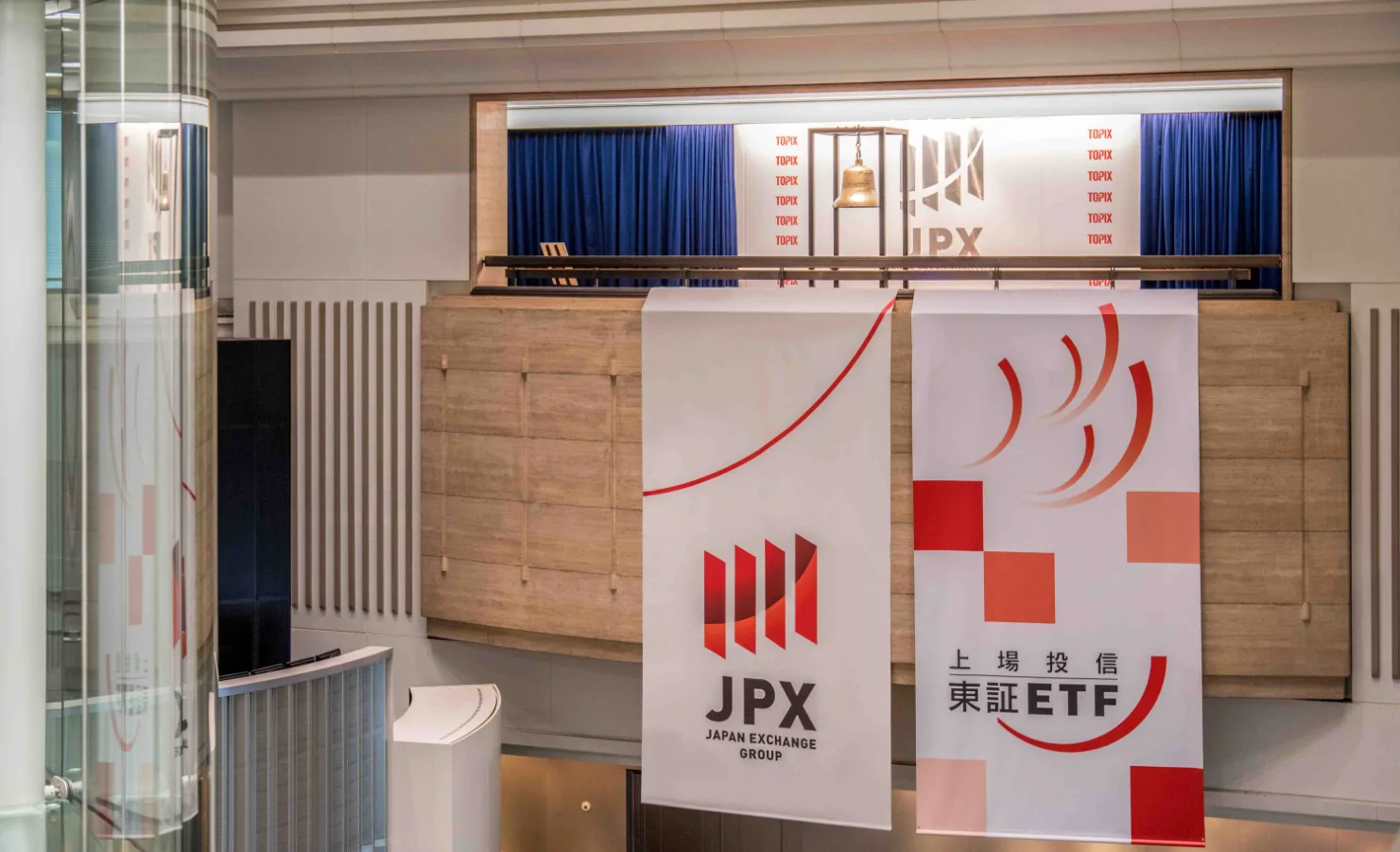 Interno della Tokyo Stock Exchange (TSE), con la campanella simbolica delle contrattazioni in evidenza. Striscioni promozionali mostrano i loghi di JPX (Japan Exchange Group) e ETF, rappresentando il mercato finanziario giapponese e le sue opportunità di investimento.