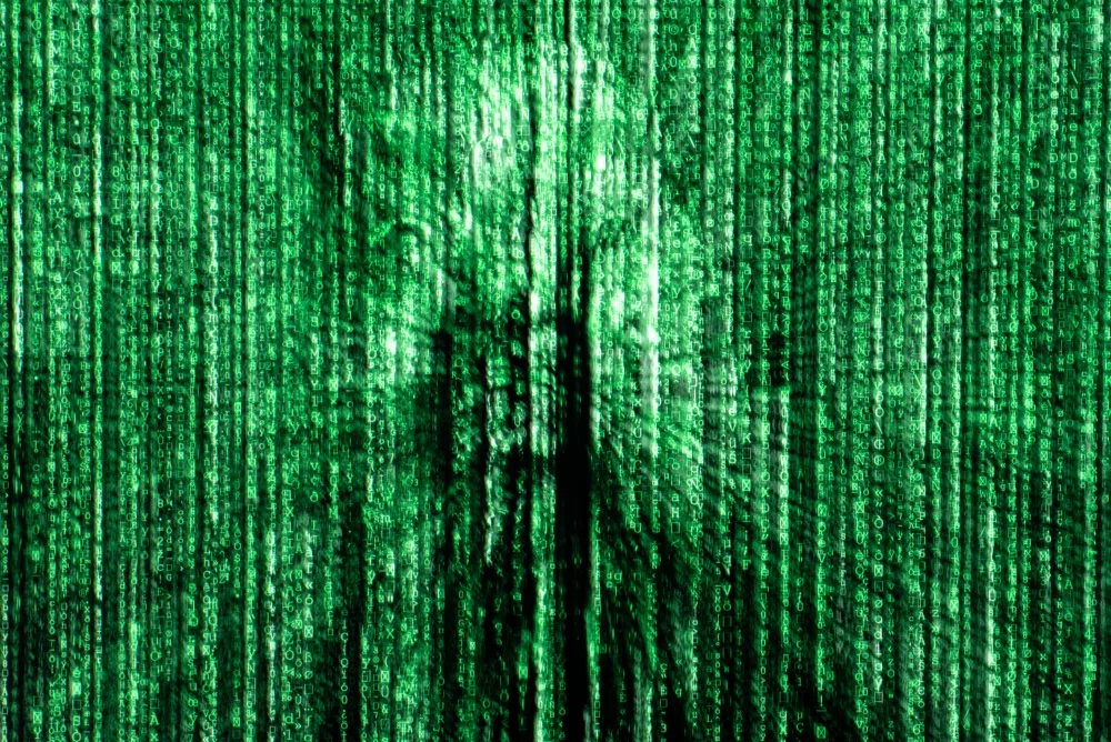 Lo schermo di un pc con file di caratteri verdi che scorrono e il riflesso di una persona sullo sfondo