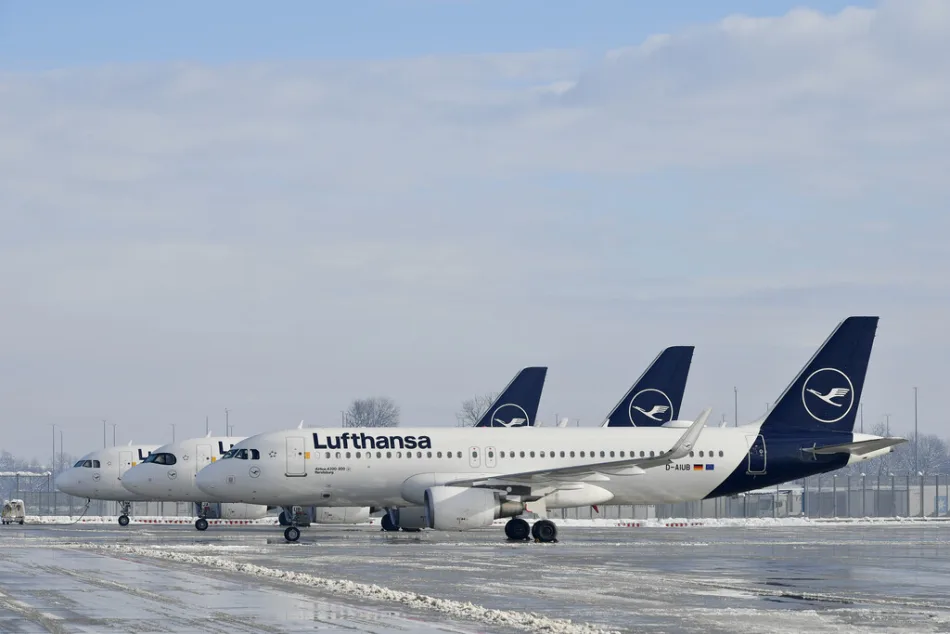 Flotta di aerei Lufthansa parcheggiati su una pista innevata in un aeroporto, con cielo parzialmente nuvoloso e condizioni invernali.