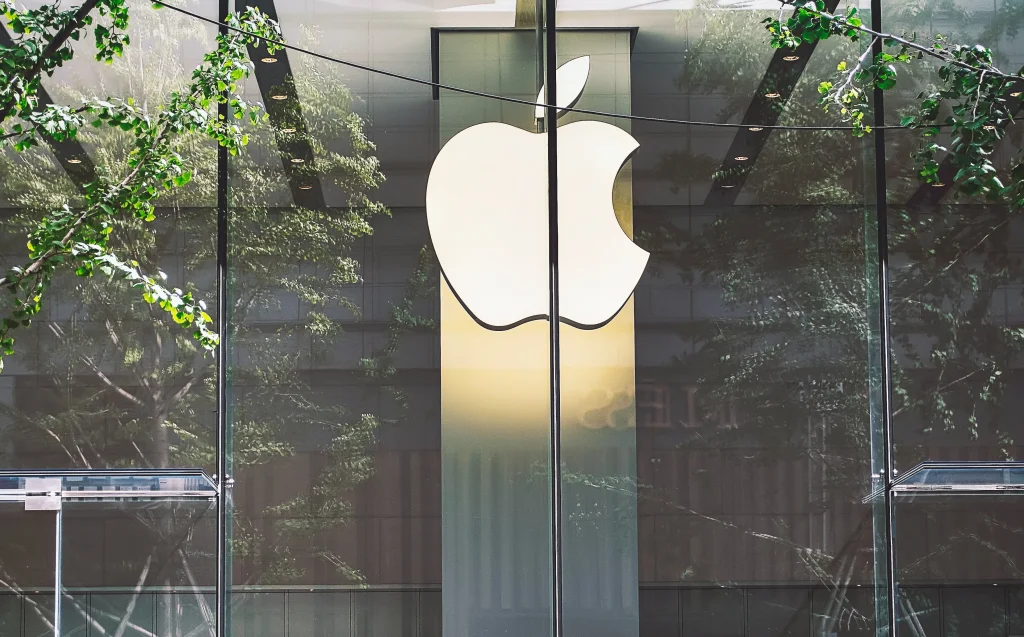 Logo Apple illuminato su facciata in vetro di un Apple Store, simbolo di tecnologia, innovazione e design nel settore tech