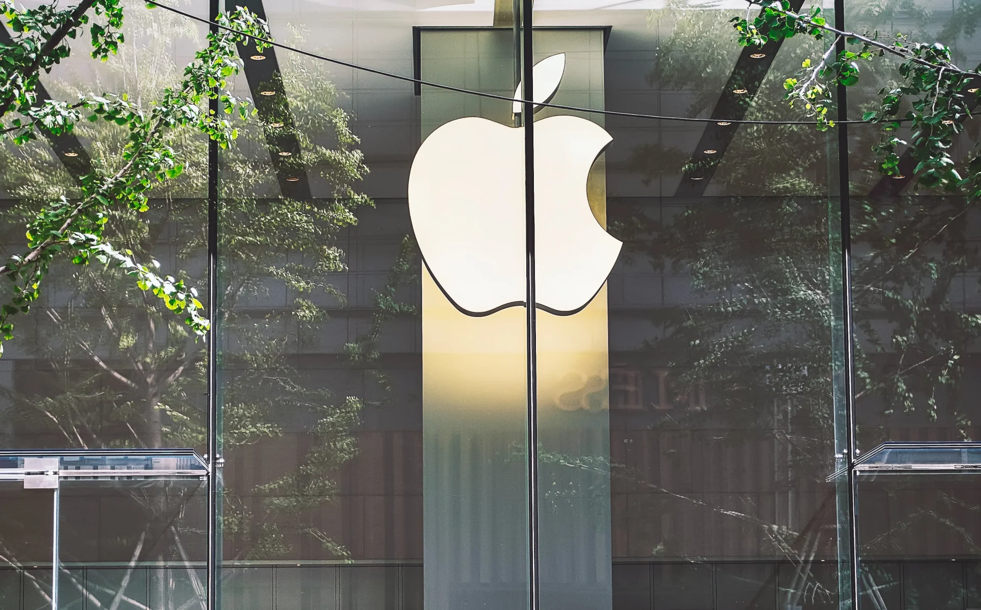 Logo Apple illuminato su facciata in vetro di un Apple Store, simbolo di tecnologia, innovazione e design nel settore tech