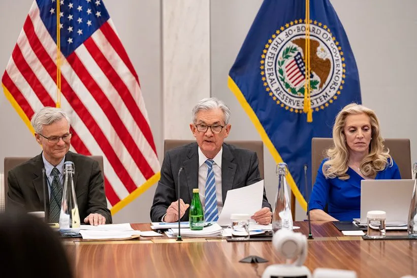 Jerome Powell presiede una riunione della Federal Reserve con bandiera USA e sigillo ufficiale sullo sfondo.