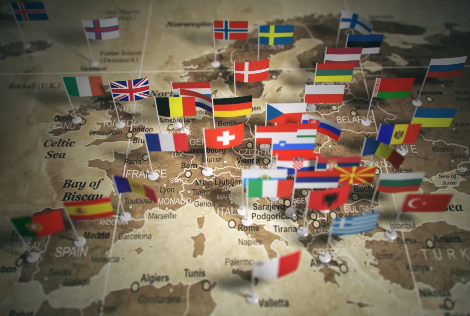 Mappa dell'Europa con bandiere di diversi Paesi posizionate su capitali e città principali, rappresentando l'unione e la diversità dell'eurozona.