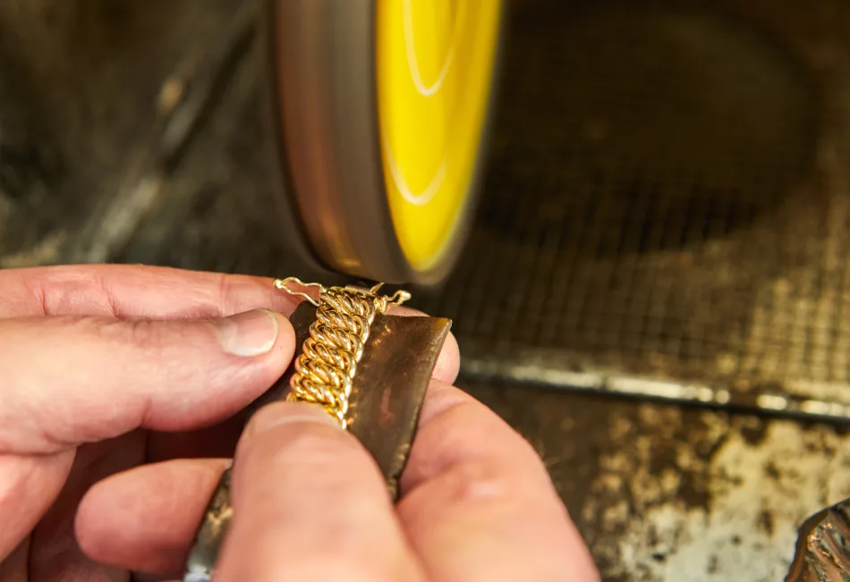 Un'immagine ravvicinata di un orafo al lavoro. Si vedono le mani che tengono un anello vicino a una macchina per la lucidatura
