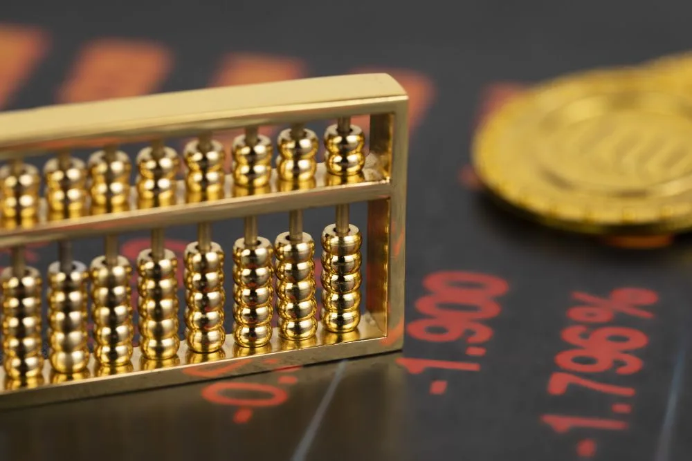 Un abaco d'oro, di piccole dimensioni, su una scrivania che riporta delle quotazioni