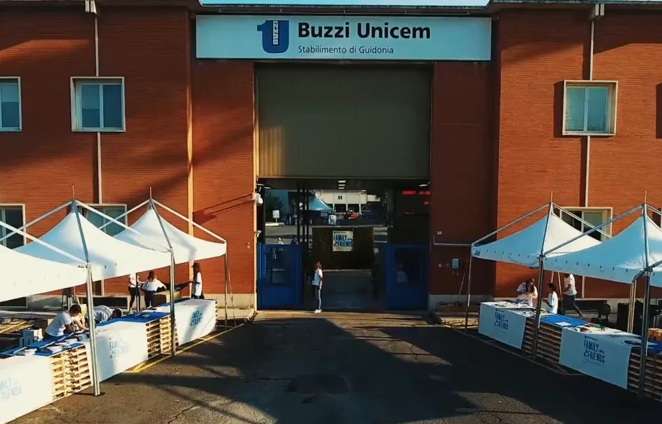 Lo stabilimento Buzzi Unicem di Guidonia, vicino a Roma. L'ingresso principale. I muri sono di colore rosso vermiglio. Sono presenti degli stand accanto al camminamento che porta all'ingresso principale, sopra il quale c'è l'insegna della società