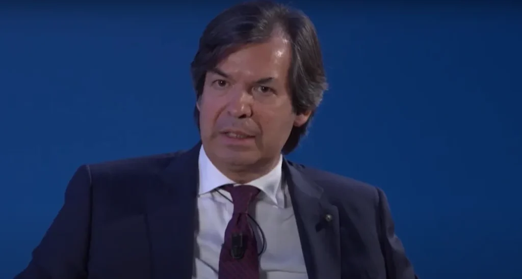 Carlo Messina, amministratore delegato di Intesa Sanpaolo nel corso di una presentazione alla stampa. La foto è un primo piano su sfondo blu. Messina indossa giacca blu scuro e cravatta rossa