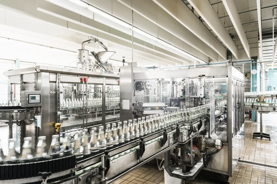 Linea di imbottigliamento industriale con macchinari moderni in acciaio inox, bottiglie di vetro in movimento su un nastro trasportatore in una fabbrica di produzione di bevande. Produzione automatizzata di bibite o acqua minerale in ambiente igienico.