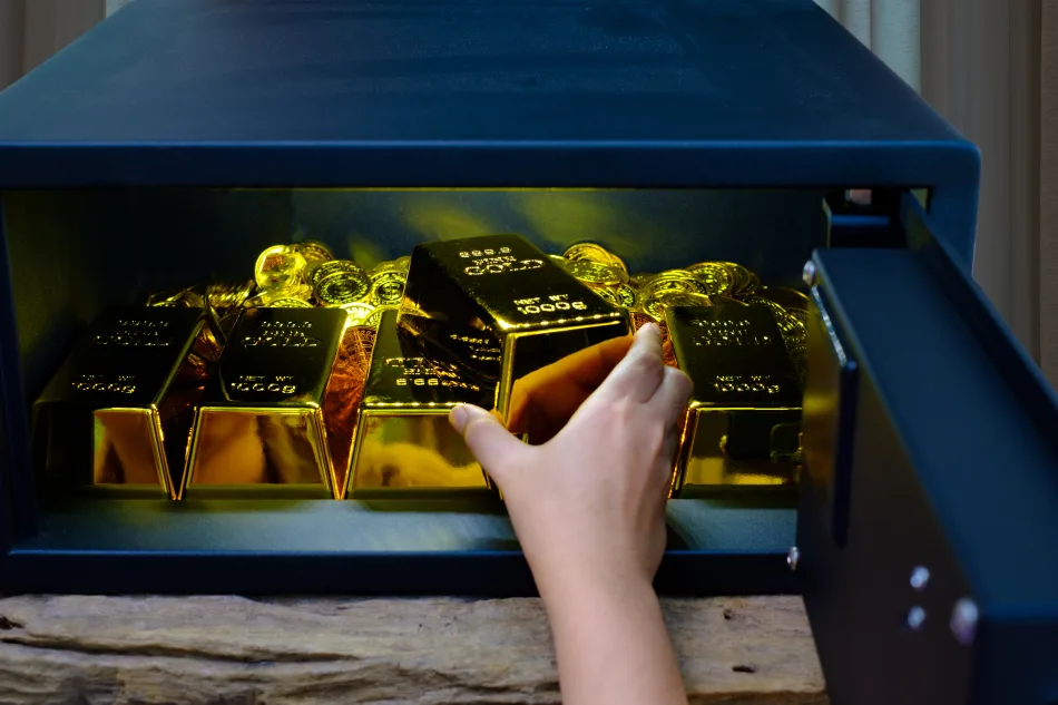 Mano che estrae lingotti d’oro da una cassaforte, rappresentando sicurezza finanziaria, investimento in metalli preziosi e protezione del patrimonio