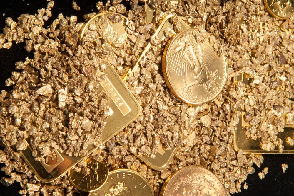 Polvere d'oro su un tavolo insieme a monete, pepite e lingotti