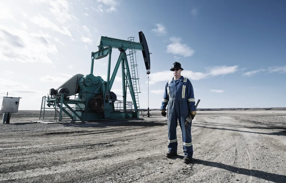 Operaio in tuta da lavoro davanti a un pozzo petrolifero in funzione in un paesaggio arido.