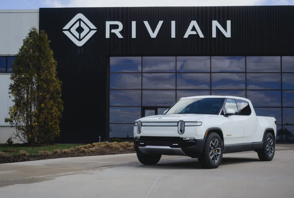 Un pick-up elettrico Rivian R1T, dal design moderno e sostenibile, è parcheggiato di fronte alla sede dell’azienda Rivian. L'immagine evidenzia il logo del marchio su un edificio dal design industriale con ampie vetrate, riflettendo l'innovazione nel settore dei veicoli elettrici.
